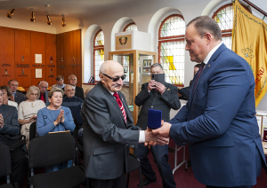 Iekšlietu ministrs Rihards Kozlovskis pasniedz piemiņas zīmi Černobiļas AES seku likvidēšanas dalībniekam. Fonā sanākušie pasākuma dalībnieki. 