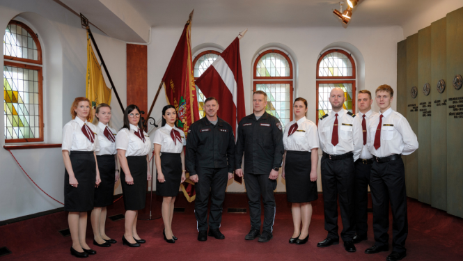 Dispečeru kopbilde Latvijas Ugunsdzēsības muzeja Slavas zālē. Dispečeriem pa vidu VUGD priekšnieka vietnieks un Vienotā kontaktu centra pārvaldes priekšnieks. Fonā Latvijas karogs.