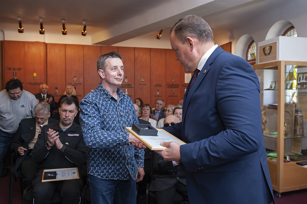 Iekšlietu ministrs Rihards Kozlovskis pasniedz piemiņas zīmi Černobiļas AES seku likvidēšanas dalībniekam. Fonā sanākušie pasākuma dalībnieki.