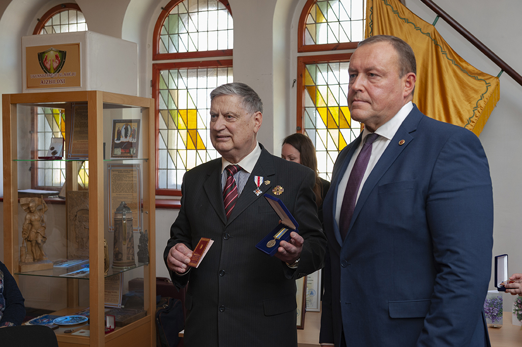 Iekšlietu ministrs Rihards Kozlovskis un Černobiļas AES seku likvidēšanas dalībnieks Latvijas Ugunsdzēsības muzeja Slavas zālē. Kreisajā pusē vitrīna ar muzeja eksponātiem. Aiz muguras redzams muzeja karogs.