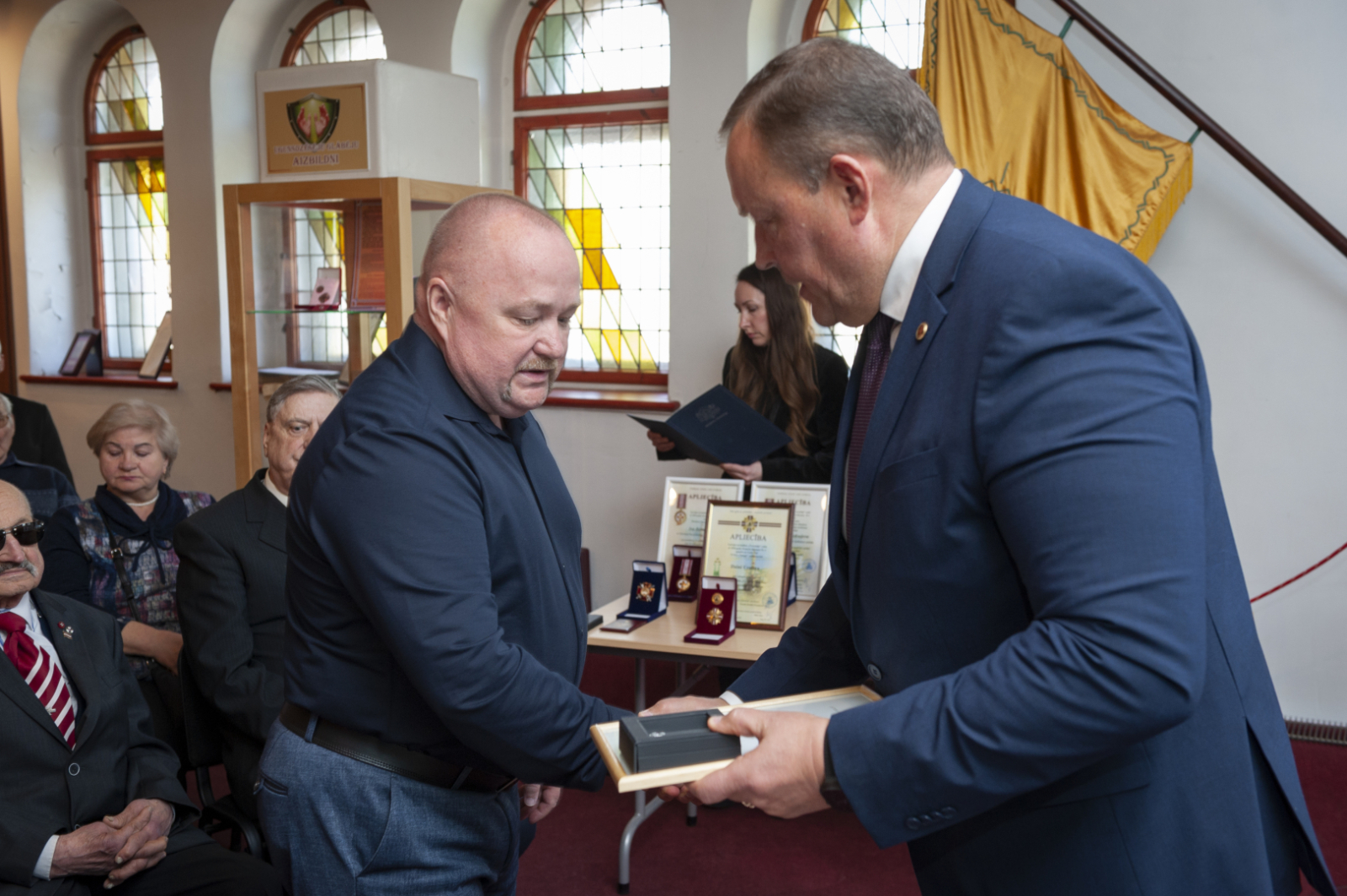 Iekšlietu ministrs Rihards Kozlovskis pasniedz piemiņas zīmi Černobiļas AES seku likvidēšanas dalībniekam. Fonā sanākušie pasākuma dalībnieki. 