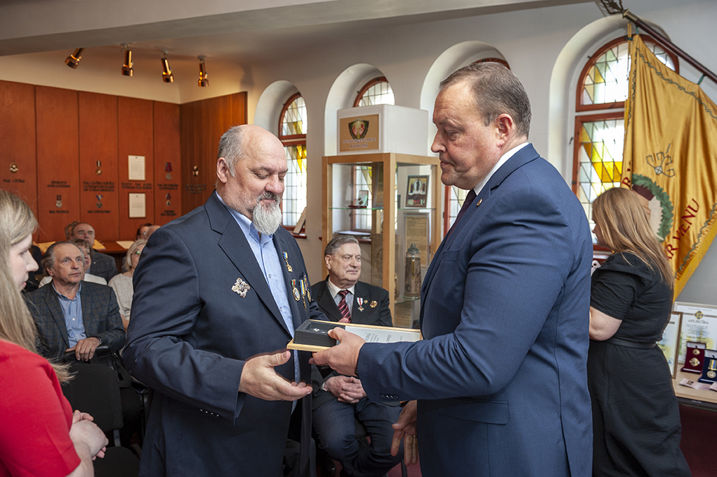 Iekšlietu ministrs Rihards Kozlovskis pasniedz piemiņas zīmi Černobiļas AES seku likvidēšanas dalībniekam. Fonā sanākušie pasākuma dalībnieki.