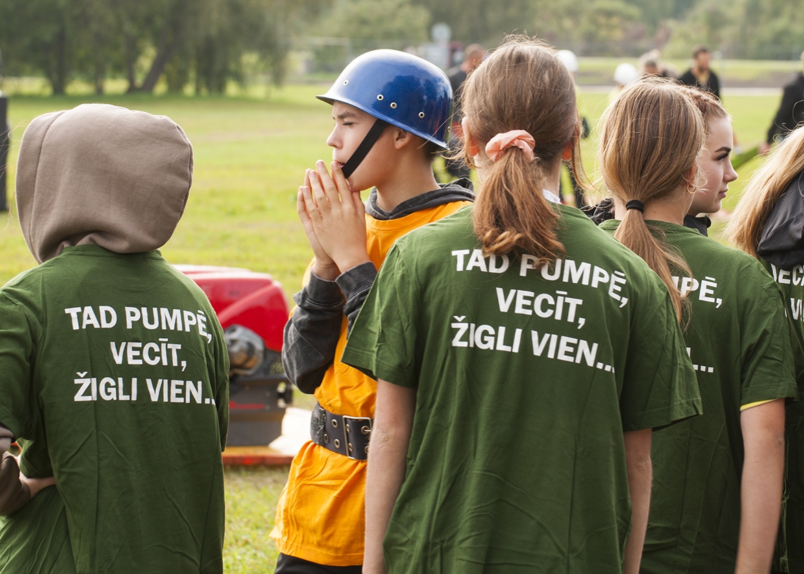 No mugurpuses uzņemti sacensību dalībnieki. Uz krekliem uzraksts Tad pumpē cecīt, žigli vien